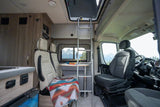 Inside a comfortable RV rental: swiveling seats, dining table, kitchen, and a ladder to a bunk, all with scenic mountain views.