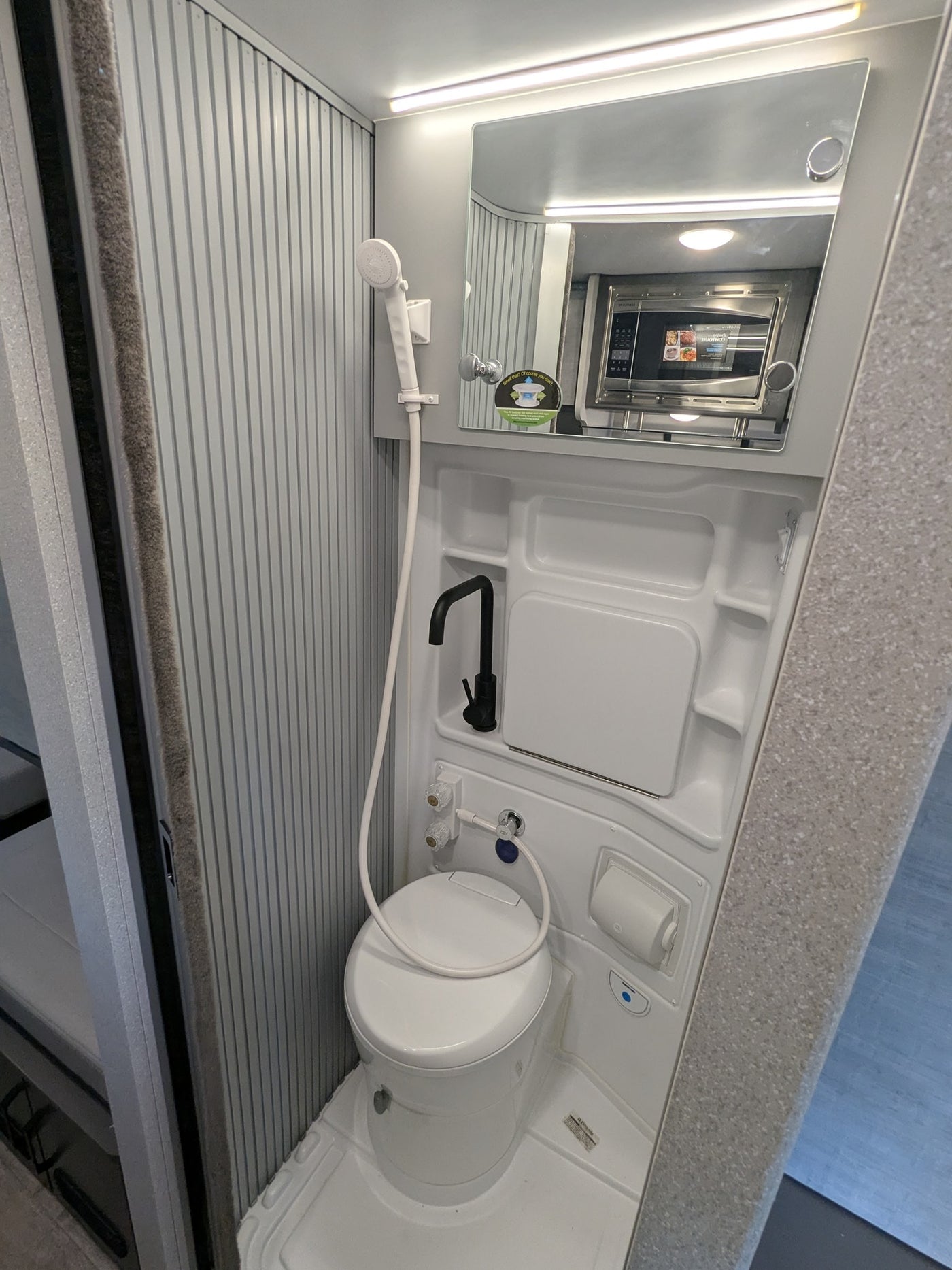 Compact RV rental bathroom with a toilet, shower, and sink. The mirror above reflects a microwave, optimizing space. — photo 11