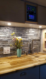Inside an RV rental: a bright, modern kitchen with butcher block counters, tile backsplash, and smart system display.