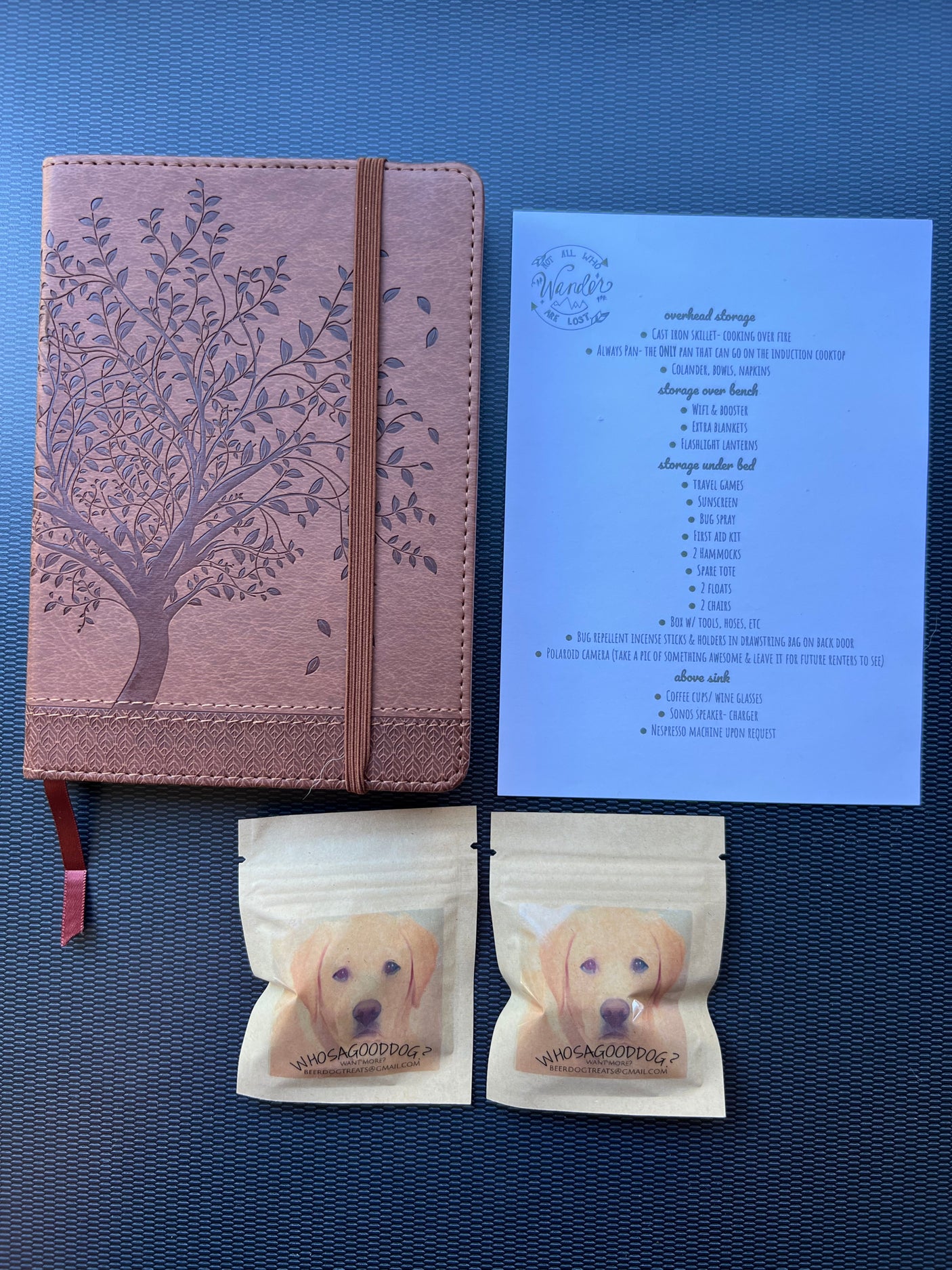 An RV rental welcome kit featuring a notebook, an amenities list for storage, and two bags of dog treats for guests.