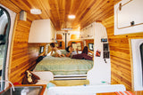 Relaxing in an rv rental: A woman reads to her child on a comfortable bed within a beautifully wood-paneled van.