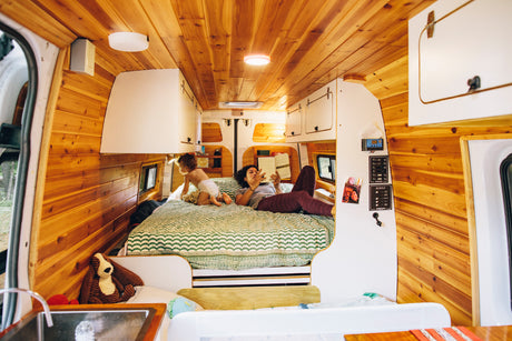 Relaxing in an rv rental: A woman reads to her child on a comfortable bed within a beautifully wood-paneled van.