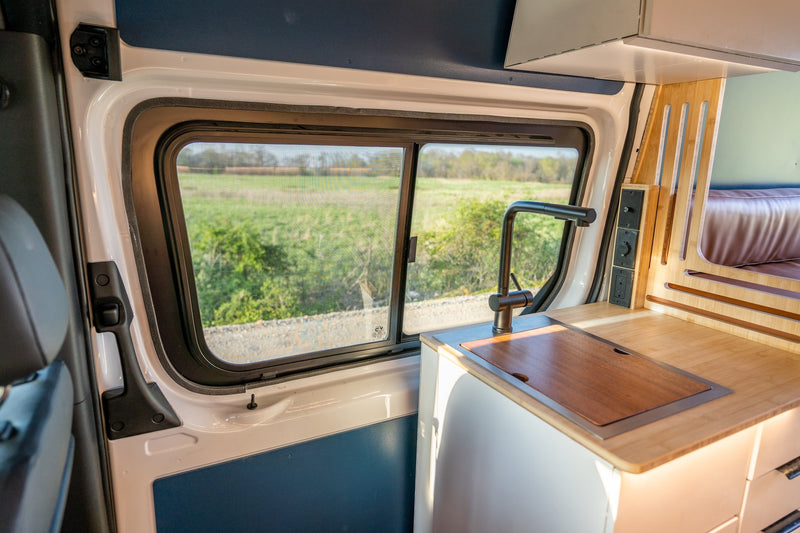 Inside a modern RV rental van: kitchen sink, counter, and a scenic window view. — photo 7