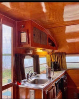 Charming RV rental kitchen with polished wood interior, stainless sink, and windows overlooking scenic views.