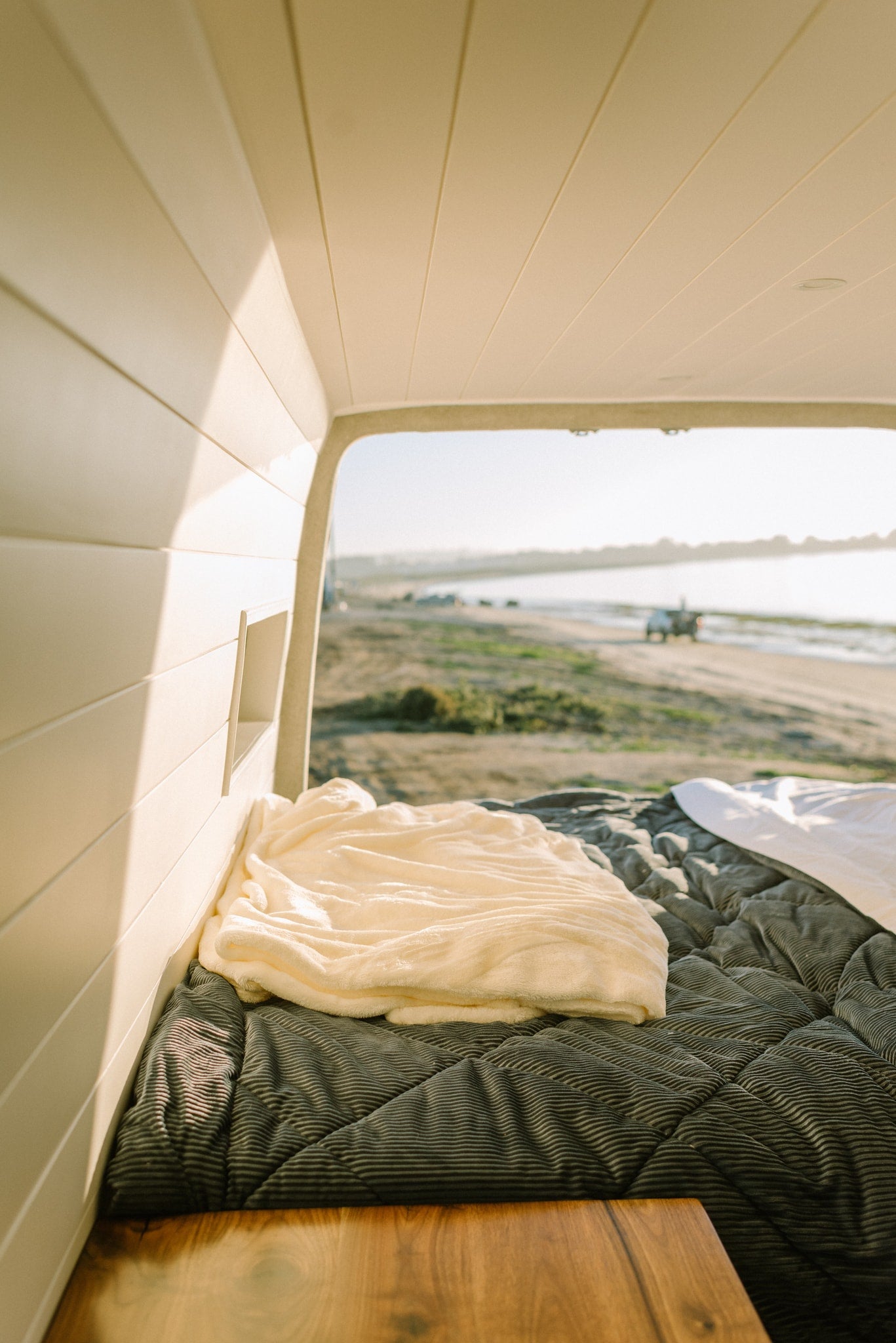 Cozy RV rental interior: a soft bed overlooks a serene beach scene, perfect for relaxing travel. — photo 8