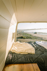 Cozy RV rental interior: a soft bed overlooks a serene beach scene, perfect for relaxing travel.