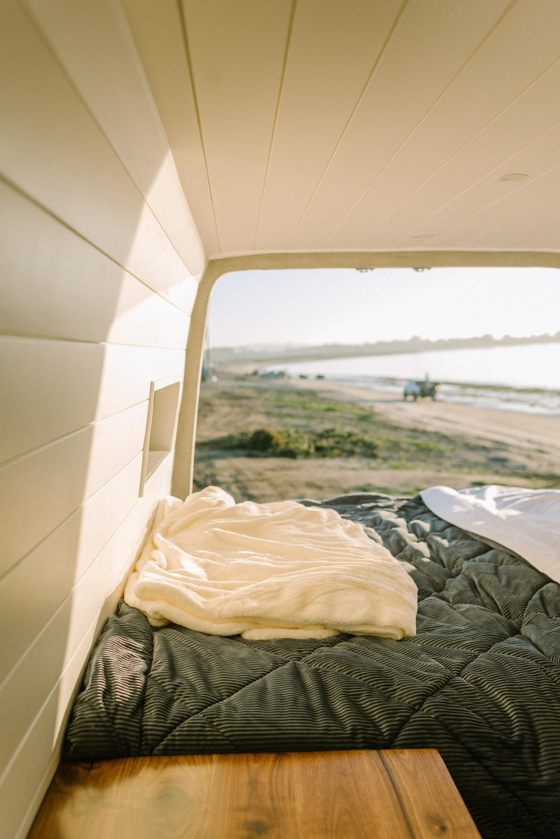 Cozy RV rental interior: a soft bed overlooks a serene beach scene, perfect for relaxing travel. — photo 8