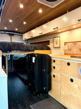 Modern RV rental interior with wood ceilings, custom cabinetry, a raised bed, and a versatile folding seat.