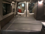 Inside an RV rental: a modern camper van with flexible grey bed cushions, integrated storage, and wide windows.
