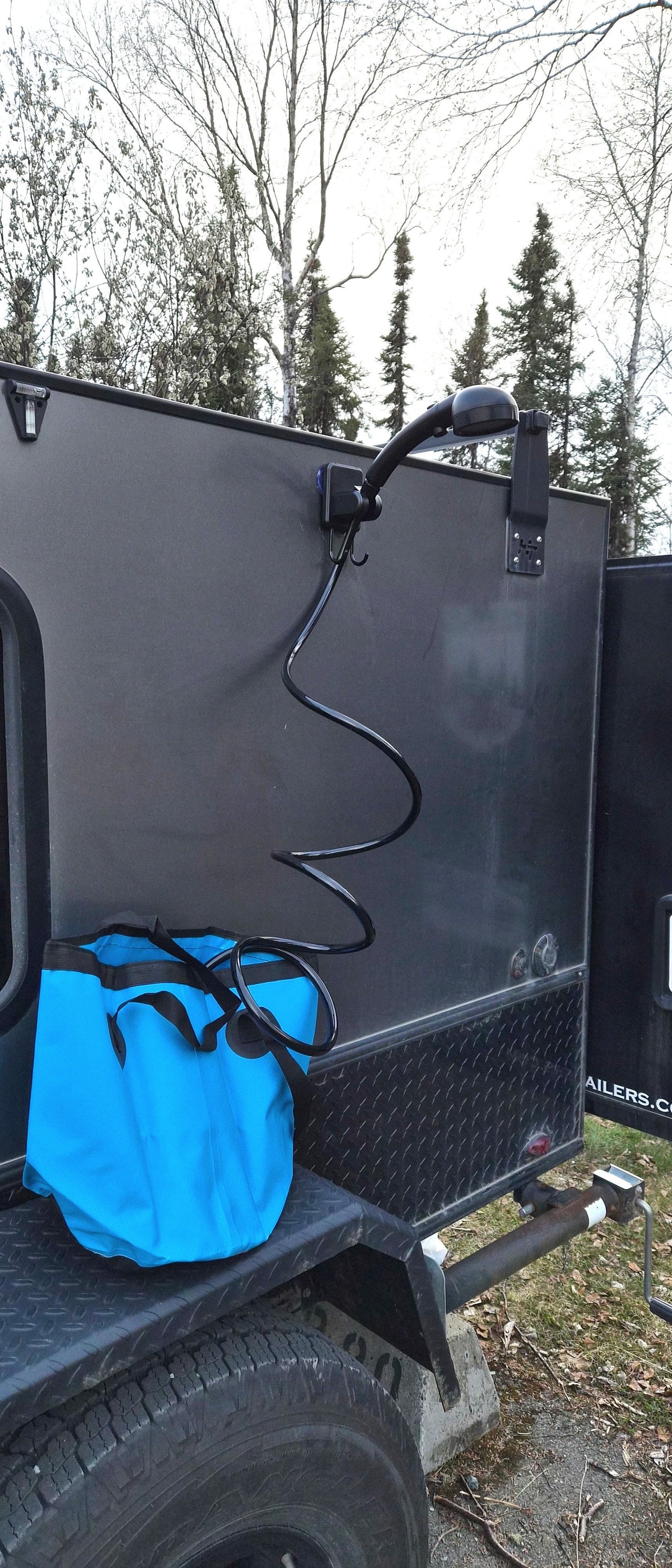 Outdoor shower on an rv rental trailer, featuring a coiled hose & blue bucket. Ideal for camping & road trips.