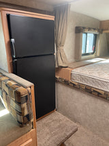 This RV rental interior showcases a Dometic refrigerator, a comfortable dinette, and a cozy bed area next to a curtained window.