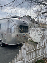 Shiny Airstream RV parked, ready for an rv rental adventure, behind a worn picket fence and leafless tree.