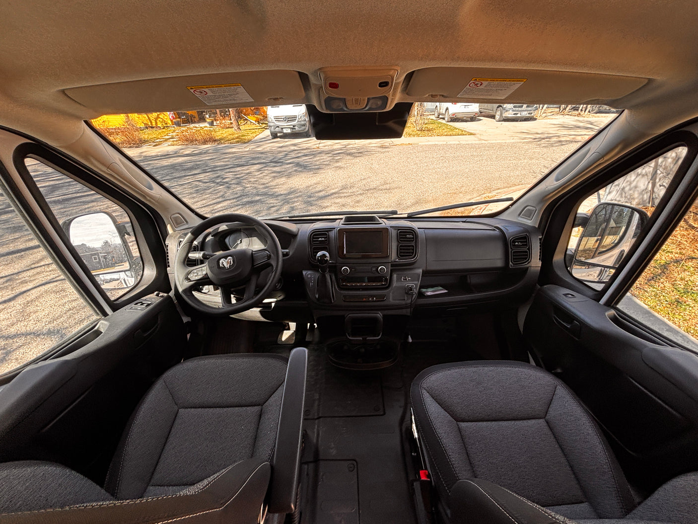 RV rental driver's view: Spacious cockpit with dashboard, steering wheel, seats, and street scene outside.