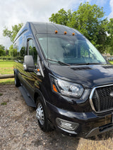 Exterior of a sleek, black high-roof custom van with amber clearance lights, parked on gravel. Ideal for your next rv rental.