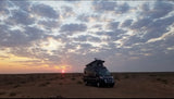Black rv rental parked in a desert at sunset, pop-top roof extended, under a cloudy sky.
