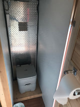 Compact RV rental bathroom featuring a portable toilet, diamond plate wall, and toilet paper dispenser. Ideal for travel.