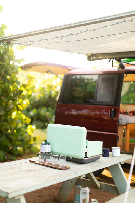 RV rental camping setup: portable stove, picnic table, and cozy van awning with string lights.