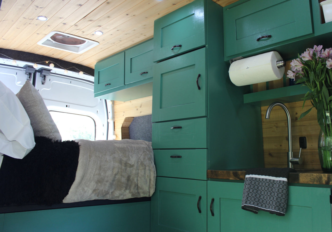 This RV rental's cozy interior features striking green cabinets, a sink, and a comfortable bed, all under a warm wooden ceiling.