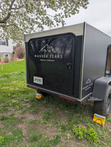 Black Wander Tears teardrop trailer, great for RV rental or camping, securely parked on grass with wheel chocks.