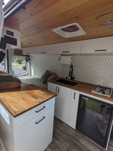 RV rental interior: modern kitchen with sink, stove, fridge, wood counters, and cozy bed area for travel.
