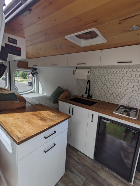 RV rental interior: modern kitchen with sink, stove, fridge, wood counters, and cozy bed area for travel.
