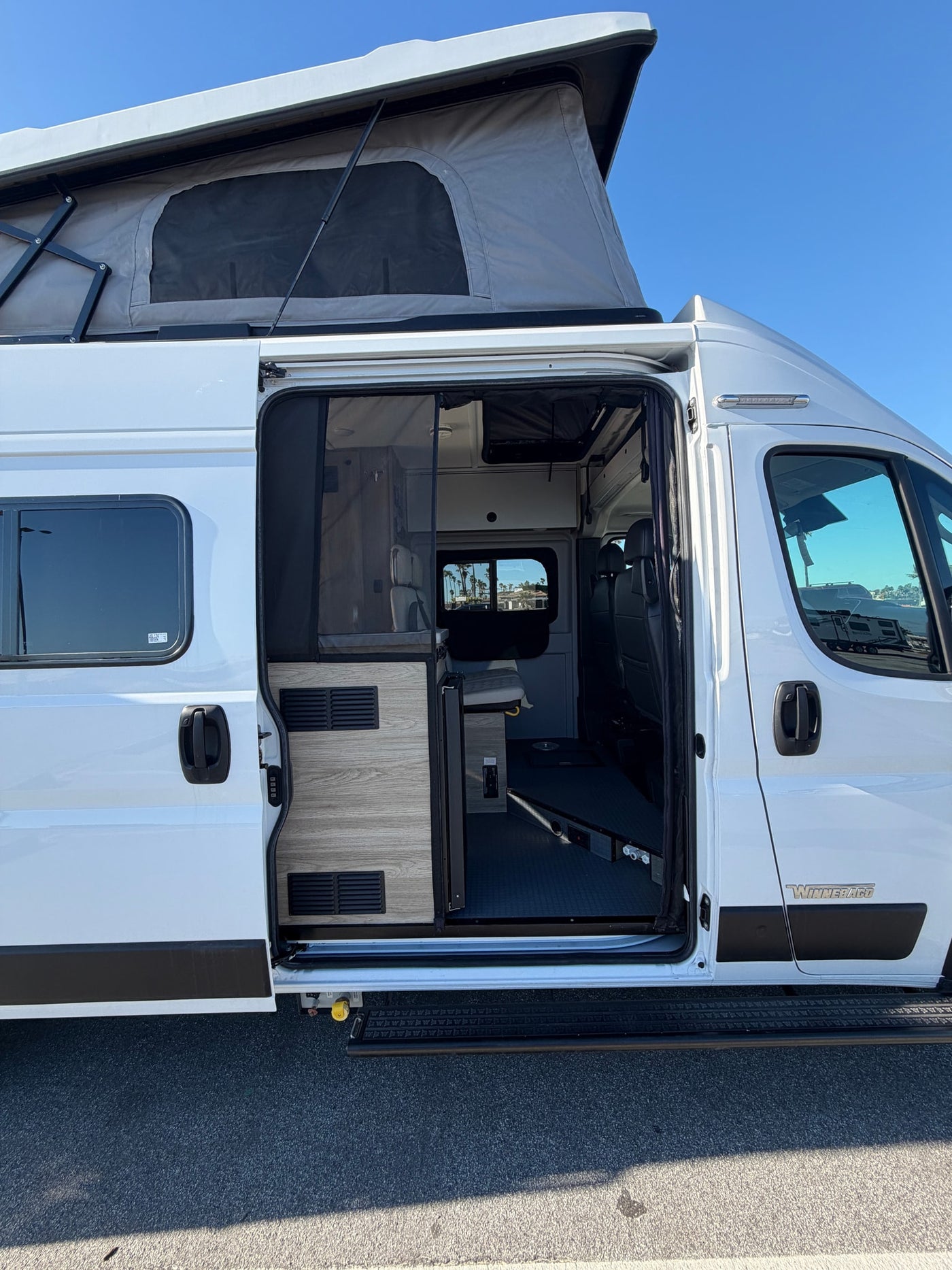  red flowers visible.|White Winnebago pop-top RV rental with open side door — photo 4