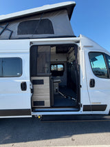White Winnebago pop-top RV rental with open side door, showing interior kitchen and seating.