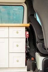 RV rental van interior: custom white cabinet, red inverter, and battery setup next to the passenger seat.