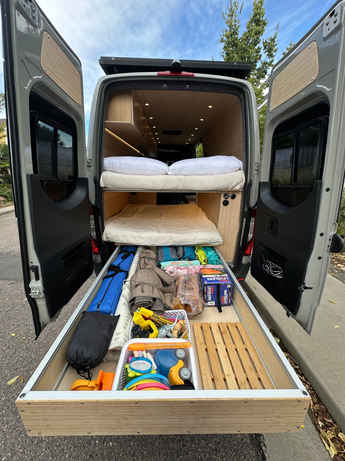 This RV rental features a camper van's custom interior with bunk beds and an extended storage drawer showing gear and toys for an adventure.