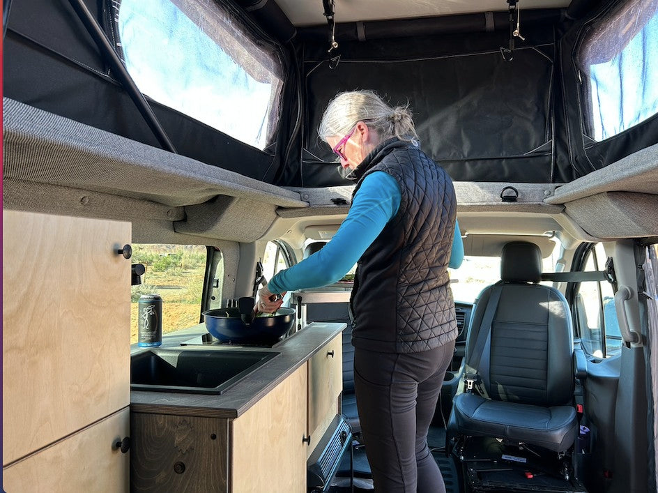 A woman cooks in a spacious RV rental van with a pop-top roof, ideal for comfortable van life adventures.