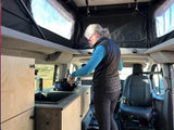 A woman cooks in a spacious RV rental van with a pop-top roof, ideal for comfortable van life adventures.