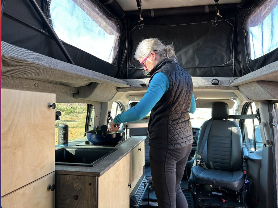 A woman cooks in a spacious RV rental van with a pop-top roof, ideal for comfortable van life adventures.
