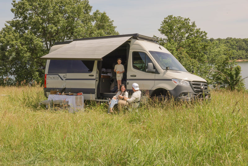 RV rental: Family relaxes by their campervan with an extended awning and outdoor meal near a lake. — photo 12