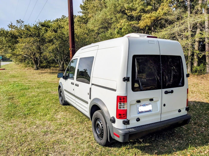 White camper van, a perfect rv rental, parked in a sunny, grassy spot with trees. Ideal for road trips and nature exploration!