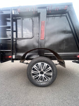 Side view of a black RV rental trailer, featuring a ladder, window, two-tone spoked wheel, and red clips for equipment.