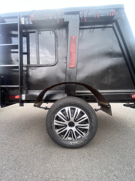 Side view of a black RV rental trailer, featuring a ladder, window, two-tone spoked wheel, and red clips for equipment.