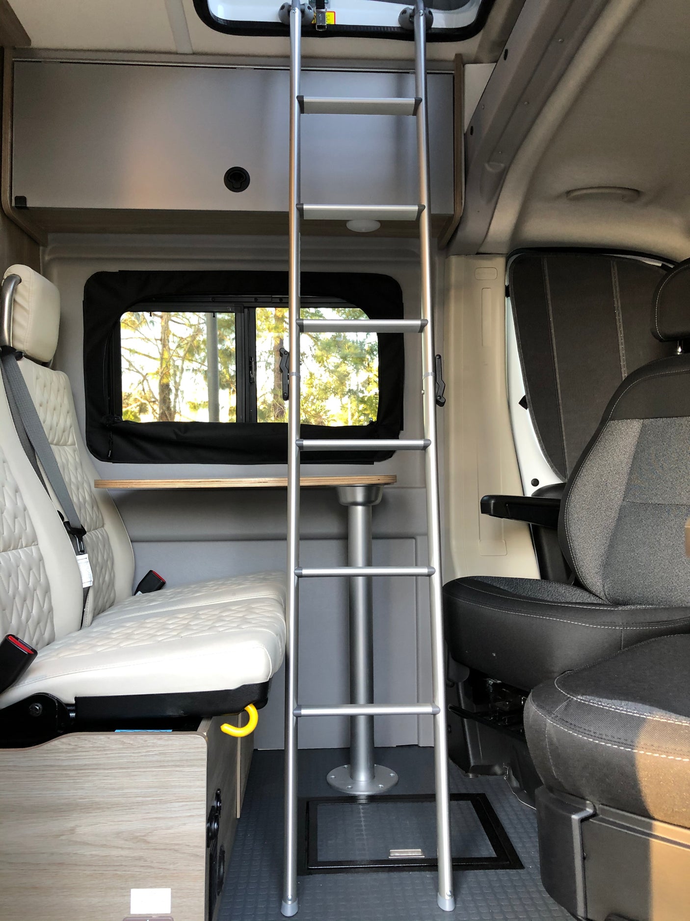 Spacious RV rental interior featuring a ladder, quilted seating, and a versatile dining table for compact living.