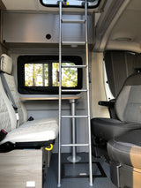 Spacious RV rental interior featuring a ladder, quilted seating, and a versatile dining table for compact living.