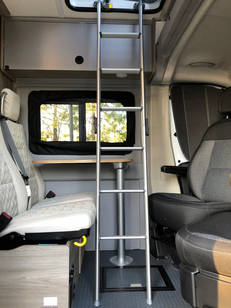 Spacious RV rental interior featuring a ladder, quilted seating, and a versatile dining table for compact living.