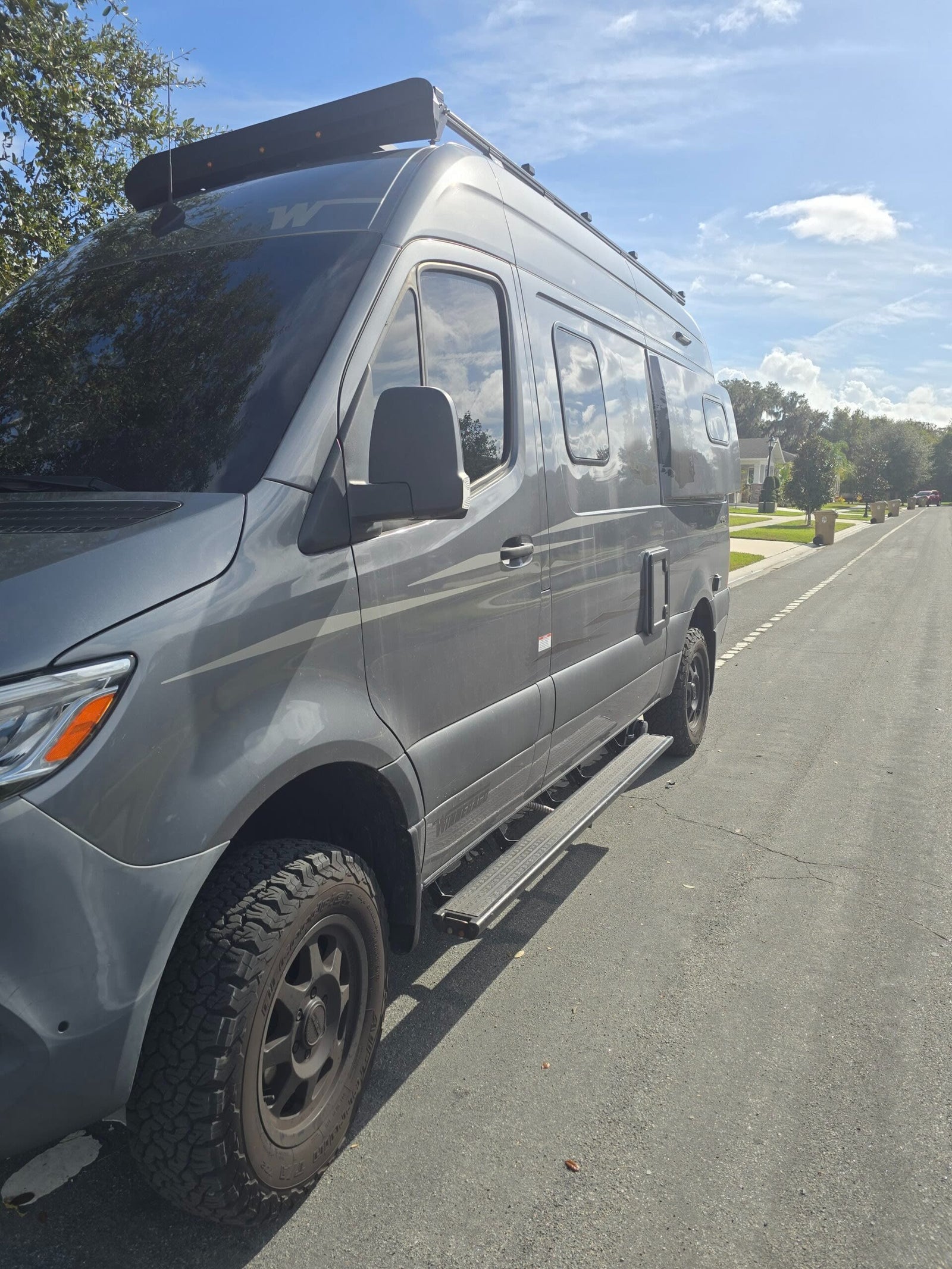 This gray camper van, perfect for rv rental, is seen parked. It features a roof rack and rugged tires for adventure.