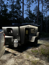 A sleek RV rental illuminated at dusk, ready for adventure. Parked with a truck in a dark forest campground.
