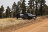Dark SUV towing a rugged camper trailer on a dirt road through a forest of pines & aspens, perfect for an RV rental adventure.
