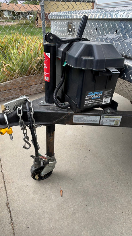 Front of an RV rental trailer, featuring a battery box, hitch, safety chains, and jack stand with wheel.