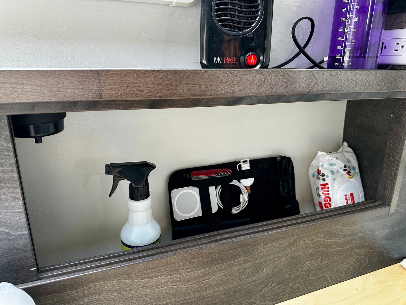 RV rental organization: compact heater, Nalgene bottle, and a cubby holding cleaning spray, tech gear, and Huggies wipes.
