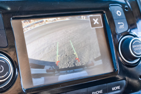 RV rental's infotainment screen displays a backup camera view with green/red parking guidelines on a dirt path.