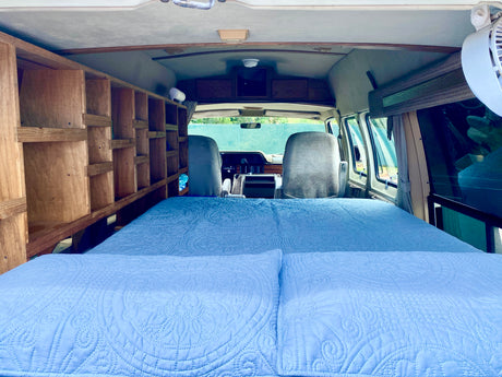 Explore this RV rental interior: a comfy bed, custom wooden shelving, and the front cabin view.