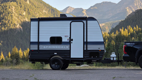 An RV rental, a Springdale travel trailer, is hitched to a truck, ready for adventure in front of majestic forested mountains.