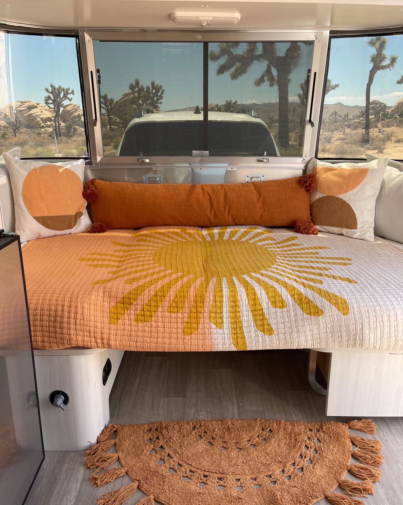  overlooking a desert landscape with Joshua trees.|Sunny RV rental interior with bright sun-themed bedding and desert views of Joshua trees through the windows.|Stylish rv rental Airstream interior: kitchenette with sink — photo 7