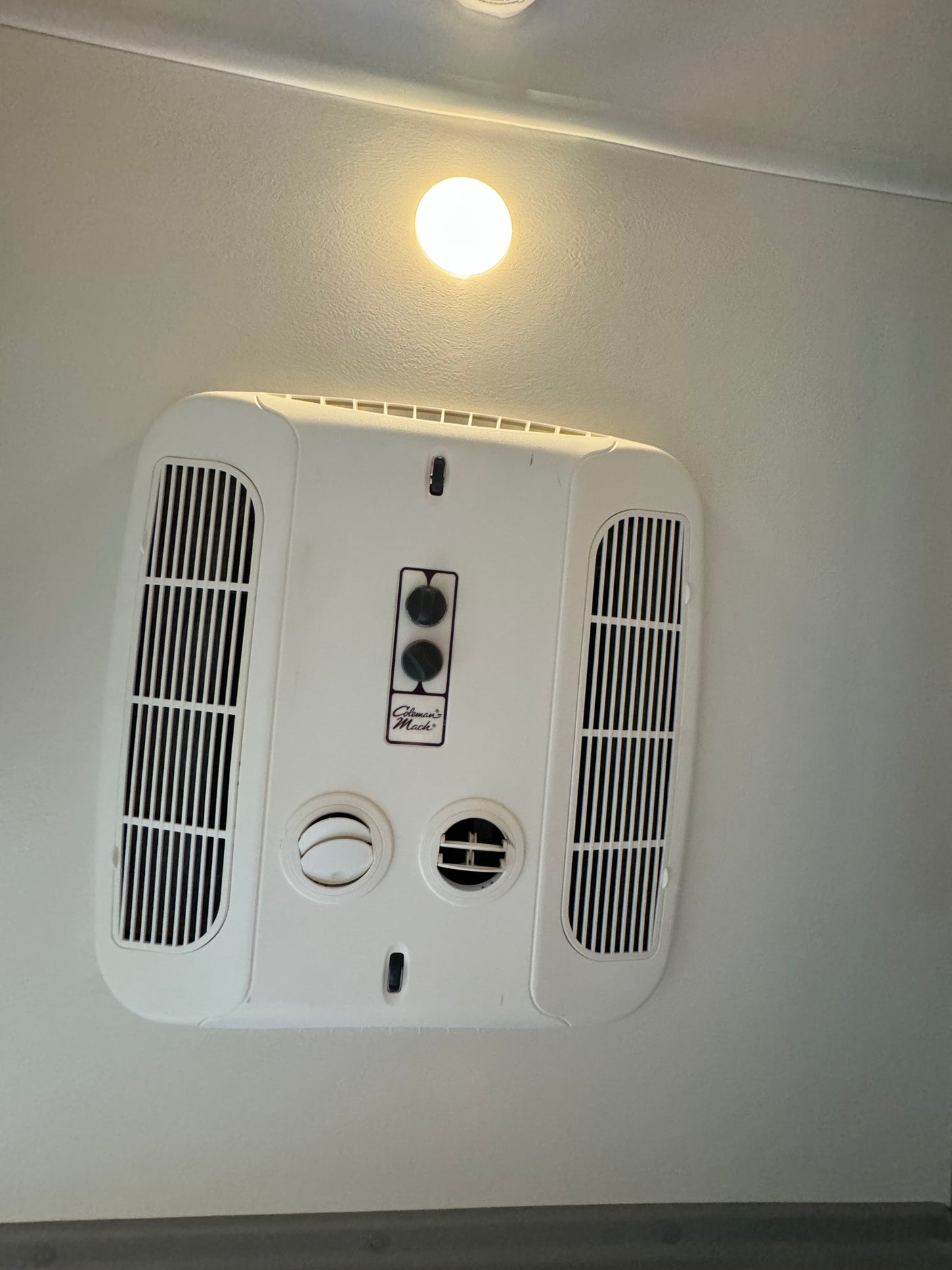An RV rental ceiling features a white Coleman-Mach air conditioning unit with adjustable vents and a bright circular light.