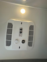 An RV rental ceiling features a white Coleman-Mach air conditioning unit with adjustable vents and a bright circular light.
